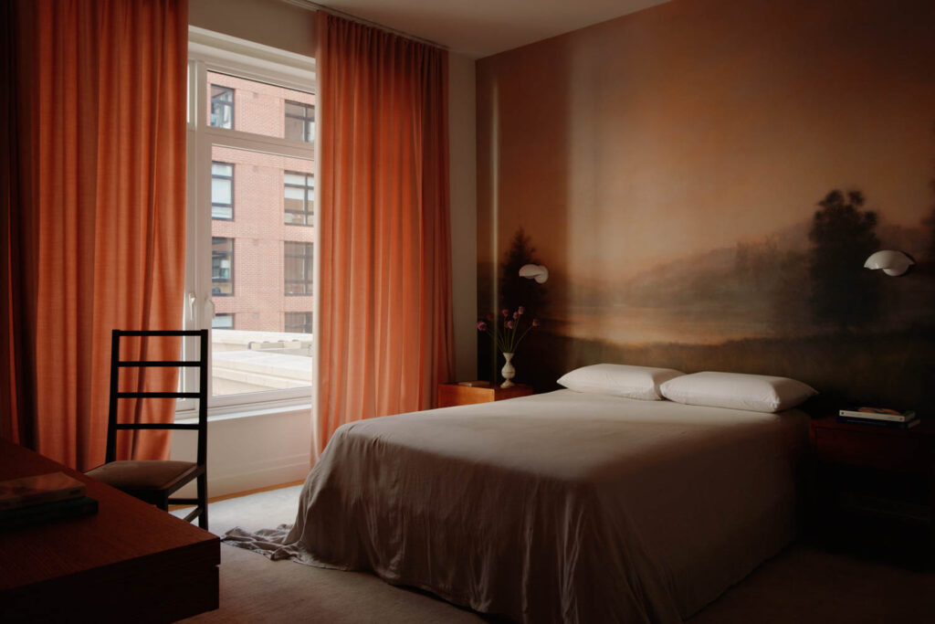 a landscape mural behind a bed in a room with orange tones