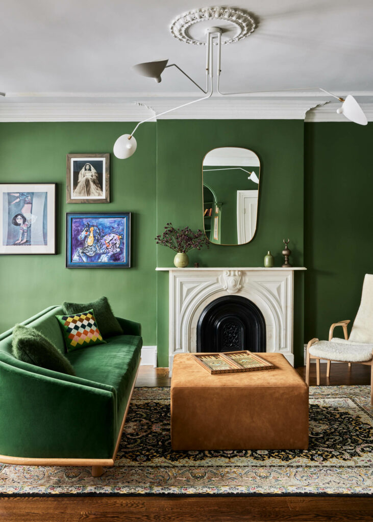 a green sofa matches the color of the walls in this library room with a white fireplace