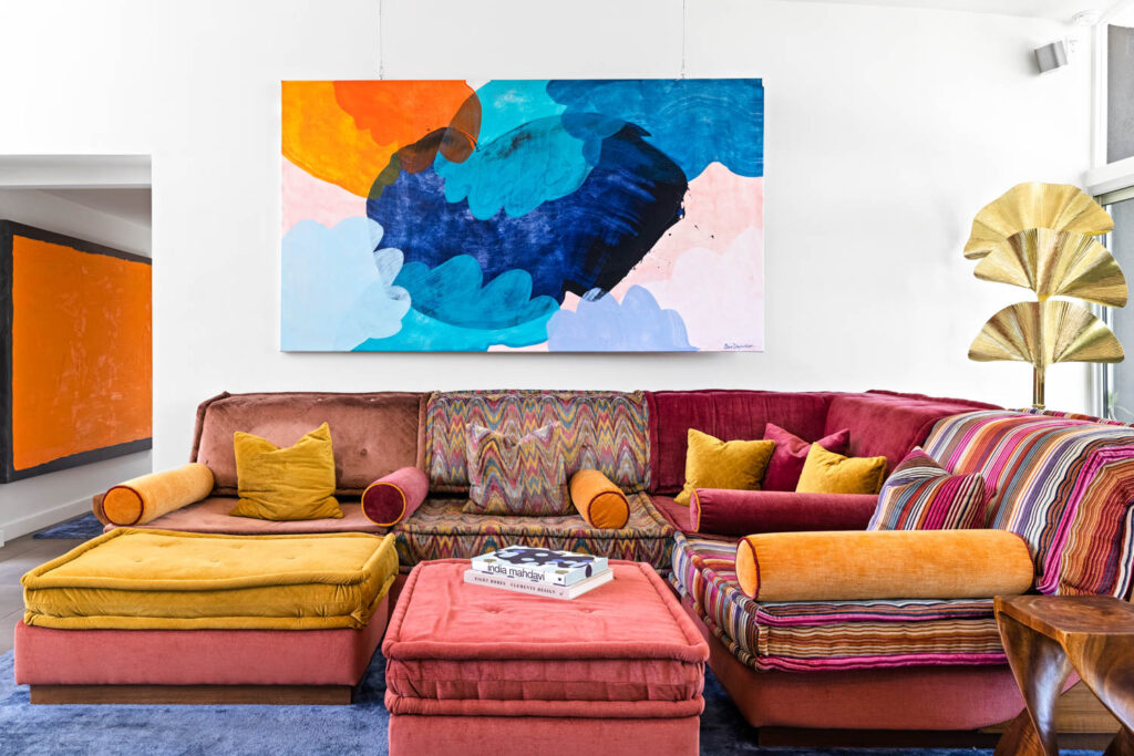 a pink and yellow multi-colored sofa and ottoman atop a blue silk rug under a colorful abstract artwork